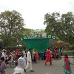 Entrance of Lahore Zoo with visitors walking in, featuring a green welcome sign and a giraffe statue.