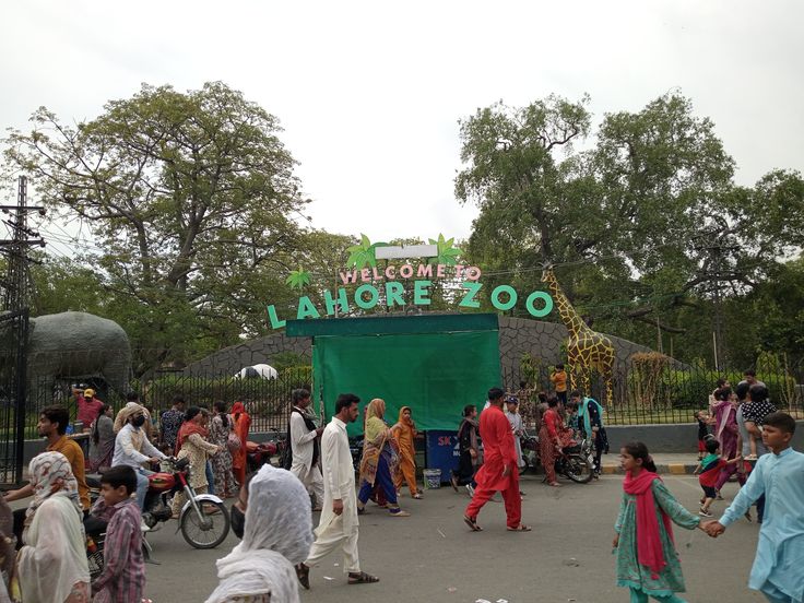 Entrance of Lahore Zoo with visitors walking in, featuring a green welcome sign and a giraffe statue.